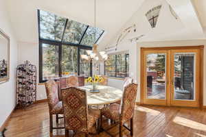 Dining area with high vaulted ceiling, a chandelier, light wood-type flooring, a skylight, and french doors