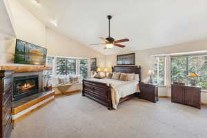 Bedroom featuring light carpet, a tile fireplace, high vaulted ceiling, and ceiling fan