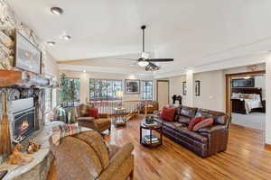 Living room featuring light wood-type flooring, vaulted ceiling, a fireplace, and ceiling fan