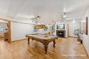 Game room featuring billiards table, light wood-style floors, a tiled fireplace, a textured ceiling, and track lighting