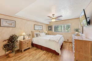 Bedroom with light wood-style floors, a textured wall, a textured ceiling, and a ceiling fan