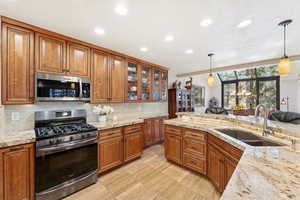 Kitchen featuring brown cabinetry, appliances with stainless steel finishes, light stone counters, and recessed lighting