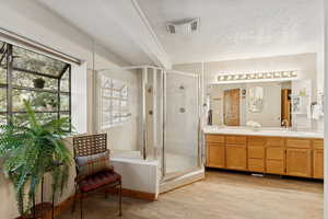 Bathroom featuring light wood-style flooring, double vanity, a textured ceiling, and a shower stall