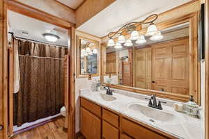 Full bathroom with a textured ceiling, double vanity, a shower with shower curtain, light wood-type flooring, and a closet