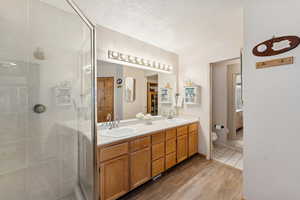 Bathroom featuring light wood-style floors, double vanity, a textured ceiling, and a stall shower