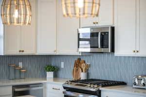Kitchen featuring white cabinetry, light stone counters, stainless steel appliances, and tasteful backsplash