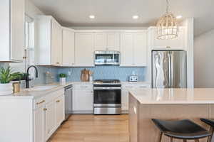 Kitchen with stainless steel appliances, decorative light fixtures, white cabinets, light stone countertops, and decorative backsplash