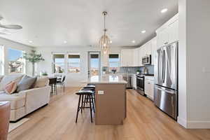 Kitchen featuring appliances with stainless steel finishes, open floor plan, a kitchen island, white cabinetry, and a kitchen breakfast bar