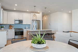 Kitchen with white cabinets, stainless steel appliances, a kitchen island, decorative backsplash, and open floor plan