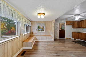 Unfurnished dining area with wood walls, ceiling fan, light wood-type flooring, and a textured ceiling