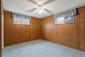 Basement featuring light colored carpet, wood walls, and ceiling fan
