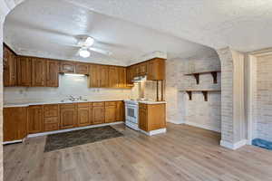 Kitchen with brick wall, light countertops, brown cabinets, white electric range, and a textured ceiling