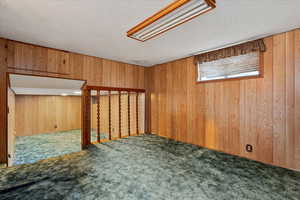 Carpeted spare room with wooden walls and a textured ceiling