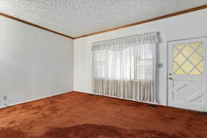 Empty room with carpet floors, a textured ceiling, crown molding, and healthy amount of natural light
