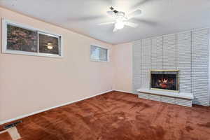 Unfurnished living room with a brick fireplace, carpet flooring, and ceiling fan