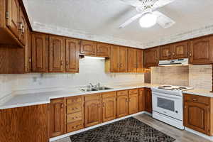 Kitchen with white electric range oven, brown cabinetry, light countertops, under cabinet range hood, and a textured ceiling
