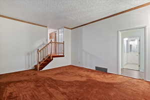 Unfurnished living room with a textured ceiling, ornamental molding, stairway, and carpet