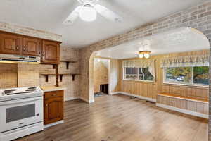 Kitchen with white range with electric cooktop, light countertops, a textured ceiling, brick wall, and brown cabinetry