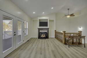 Living area featuring vaulted ceiling, light wood-style flooring, a lit fireplace, ceiling fan, and recessed lighting