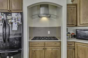 Kitchen featuring black appliances, exhaust hood, brown cabinets, and decorative backsplash