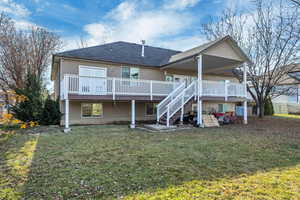 Back of house with a deck, roof with shingles, stairway, and a lawn