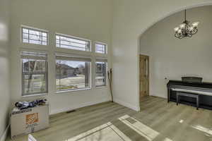 Entrance foyer featuring a towering ceiling, a chandelier, arched walkways, and light wood finished floors