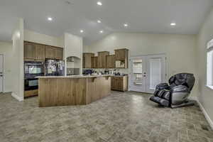 Kitchen with a kitchen bar, black appliances, a center island with sink, light countertops, and high vaulted ceiling