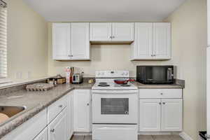 Kitchen featuring white electric range, white cabinets, black microwave, and light tile patterned floors