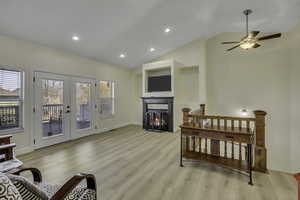 Living room featuring a warm lit fireplace, french doors, recessed lighting, light wood-style flooring, and ceiling fan