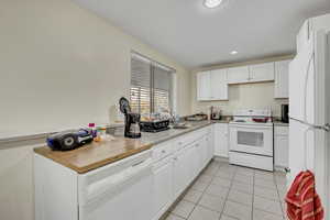 Kitchen featuring white appliances, white cabinets, light tile patterned flooring, and recessed lighting