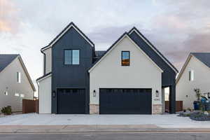 Modern inspired farmhouse featuring board and batten siding, a garage, stone siding, and driveway
