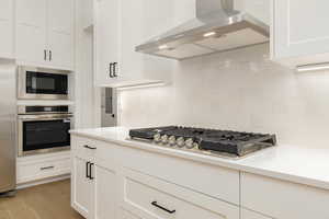 Kitchen featuring range hood, stainless steel appliances, white cabinets, decorative backsplash, and light wood finished floors