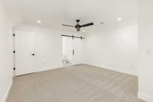Unfurnished bedroom with recessed lighting, a barn door, ceiling fan, light colored carpet, and ensuite bathroom