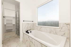 Full bathroom with light marble finish floors, a bath, a marble finish shower, and a spacious closet