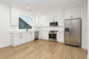 Kitchen with stainless steel appliances, white cabinetry, light wood finished floors, and recessed lighting