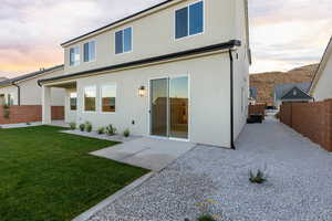 Back of property at dusk with a fenced backyard, stucco siding, and a patio area
