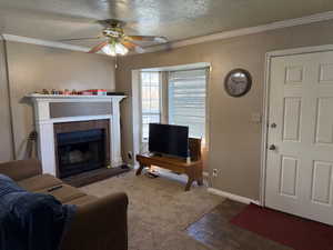 Living room featuring a textured ceiling, a brick fireplace, ornamental molding, a textured wall, and ceiling fan