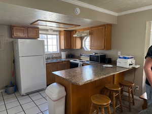 Kitchen with white appliances, a peninsula, a kitchen bar, a textured ceiling, and brown cabinetry