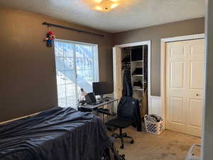 Carpeted bedroom featuring a textured ceiling, two closets, and a desk