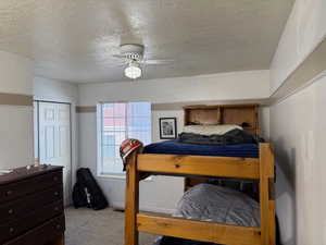 Carpeted bedroom featuring a textured ceiling, a closet, and a ceiling fan