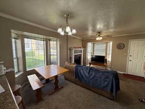 Living area featuring a textured ceiling, a tile fireplace, crown molding, a chandelier, and a ceiling fan