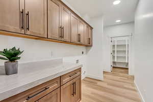 Bar area featuring light stone countertops, light wood-type flooring, recessed lighting, and brown cabinetry