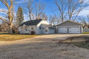 View of front facade featuring a garage, an outdoor structure, concrete driveway, a chimney, and a shingled roof.