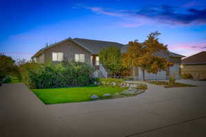 View of property hidden behind natural elements with brick siding, a front lawn, concrete driveway, and a shingled roof