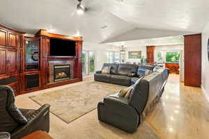 Living area featuring a fireplace, lofted ceiling, light wood-type flooring, and ceiling fan