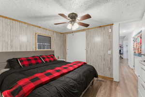 Bedroom with wood walls, light wood finished floors, a closet, a ceiling fan, and a textured ceiling