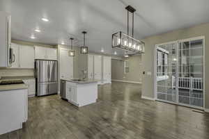 Kitchen with a kitchen island with sink, stainless steel appliances, open floor plan, pendant lighting, and white cabinets