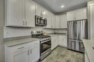 Kitchen featuring stainless steel appliances, light stone countertops, white cabinetry, light wood-style floors, and recessed lighting