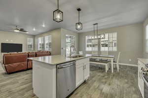 Kitchen featuring appliances with stainless steel finishes, white cabinetry, pendant lighting, light stone countertops, and light wood-style floors
