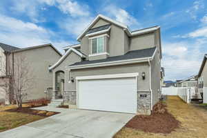 View of front facade featuring stone siding, stucco siding, concrete driveway, and a garage